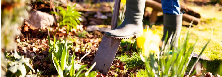 Person mit Gummistiefeln und Spaten im Garten